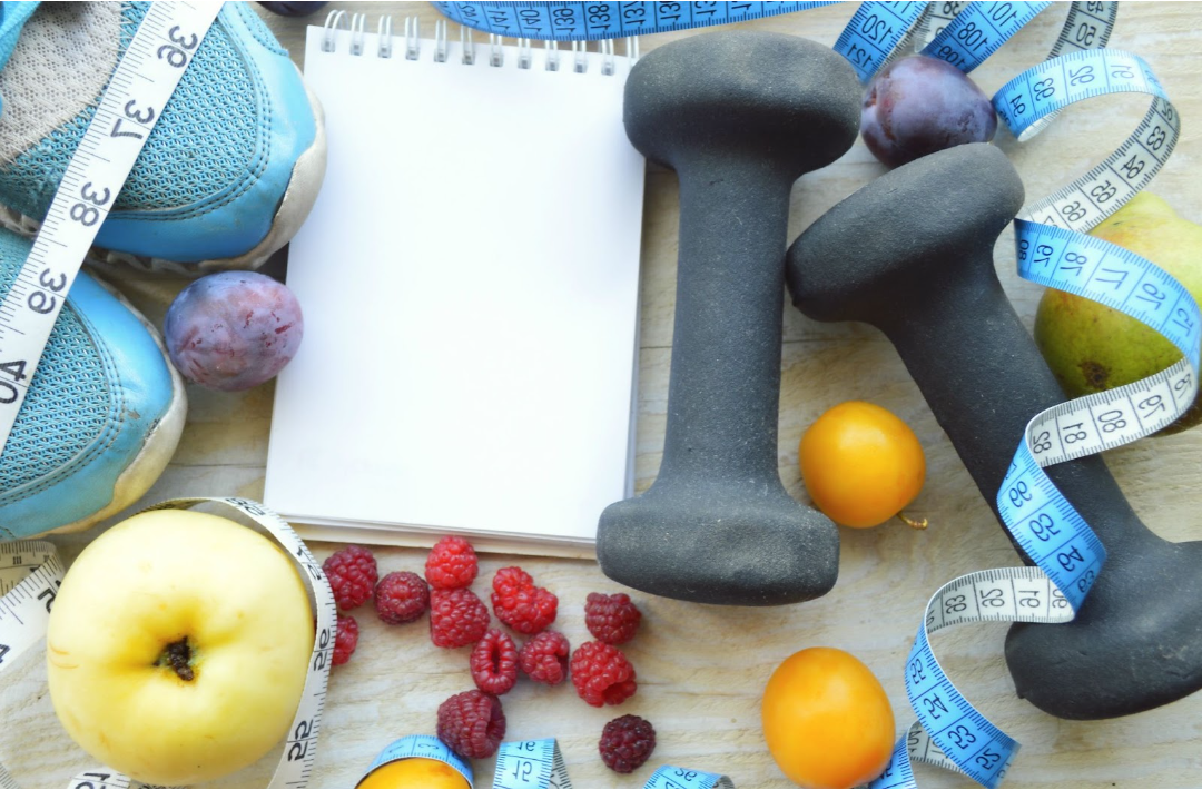 Table covered in items that help with weight loss including healthy foods, running shoes, and dumbbells.