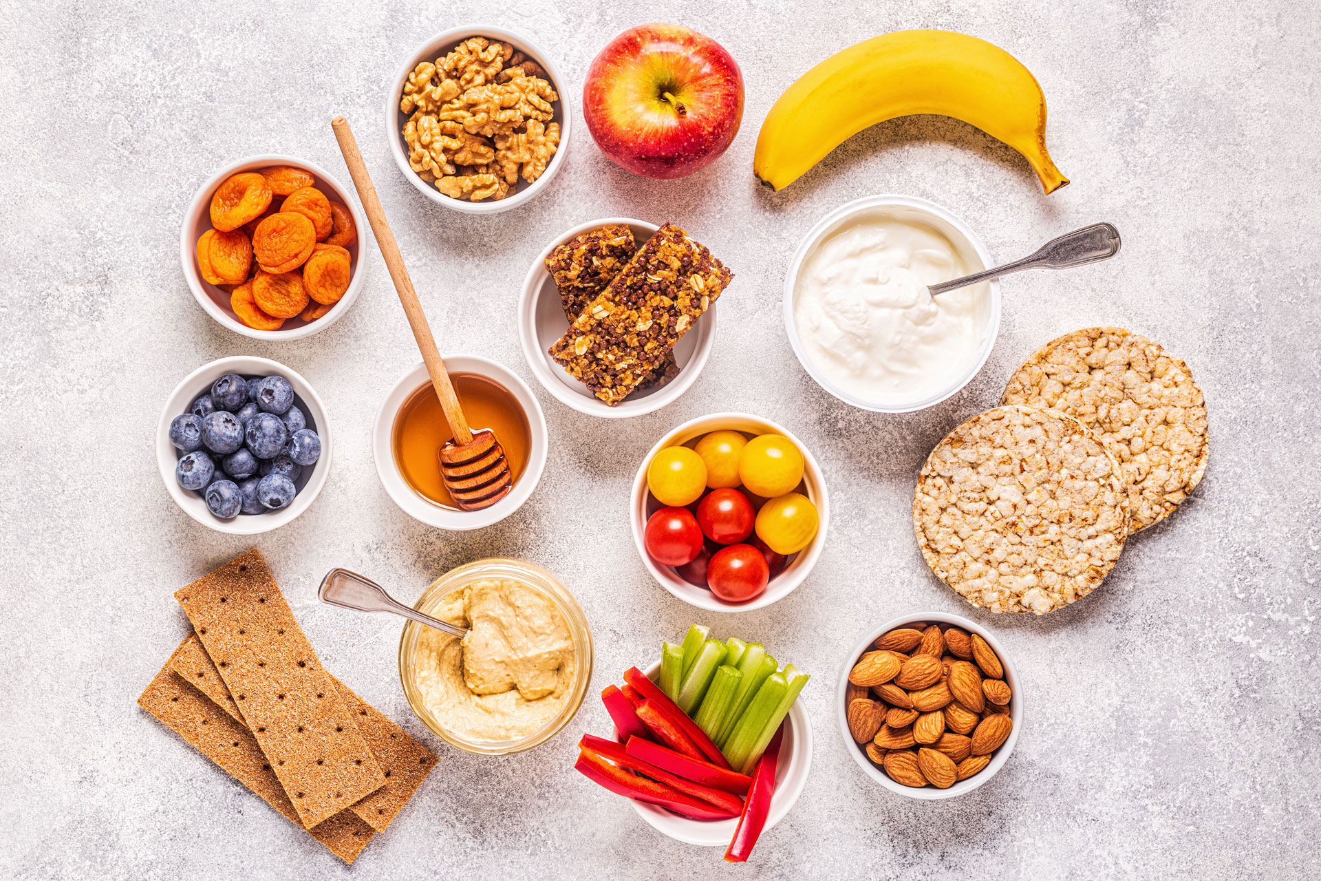 Healthy assortment of snacks that are good for losing weight including fruits, vegetables, nuts, honey, wheat based snacks, and puffed rice cakes. 