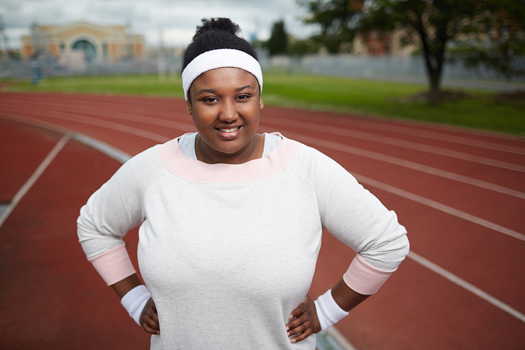 A woman wearing a long sleeve top and sweatbands stands on a track with her hands on her hips.